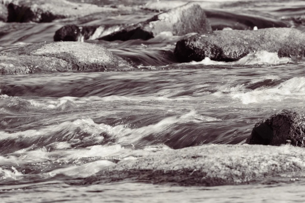 Fine art black and white close-up of flowing water moving around granite rocks in the Lower Saluda River, Columbia, South Carolina