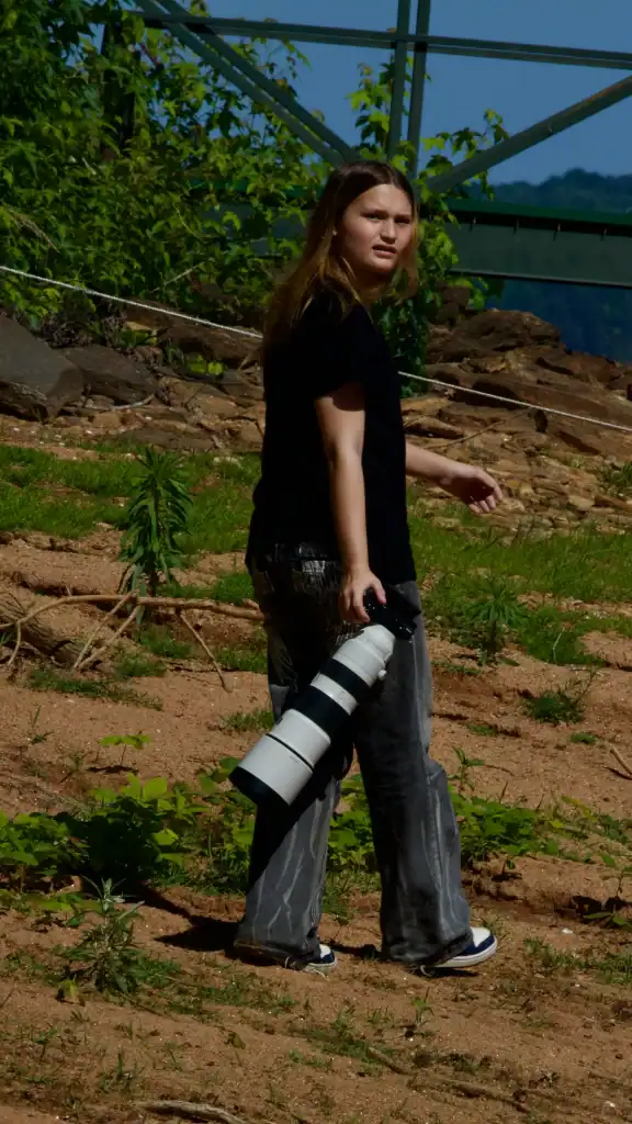 Avery carrying a Sony telephoto lens while exploring outdoors as part of the father-daughter wildlife project behind Apex Exposure Media.